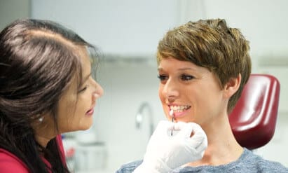 Praxisassistenz gleicht in der Praxisklinik Herne die Zahnfarbe einer Patientin für eine Veneer-Behandlung ab.